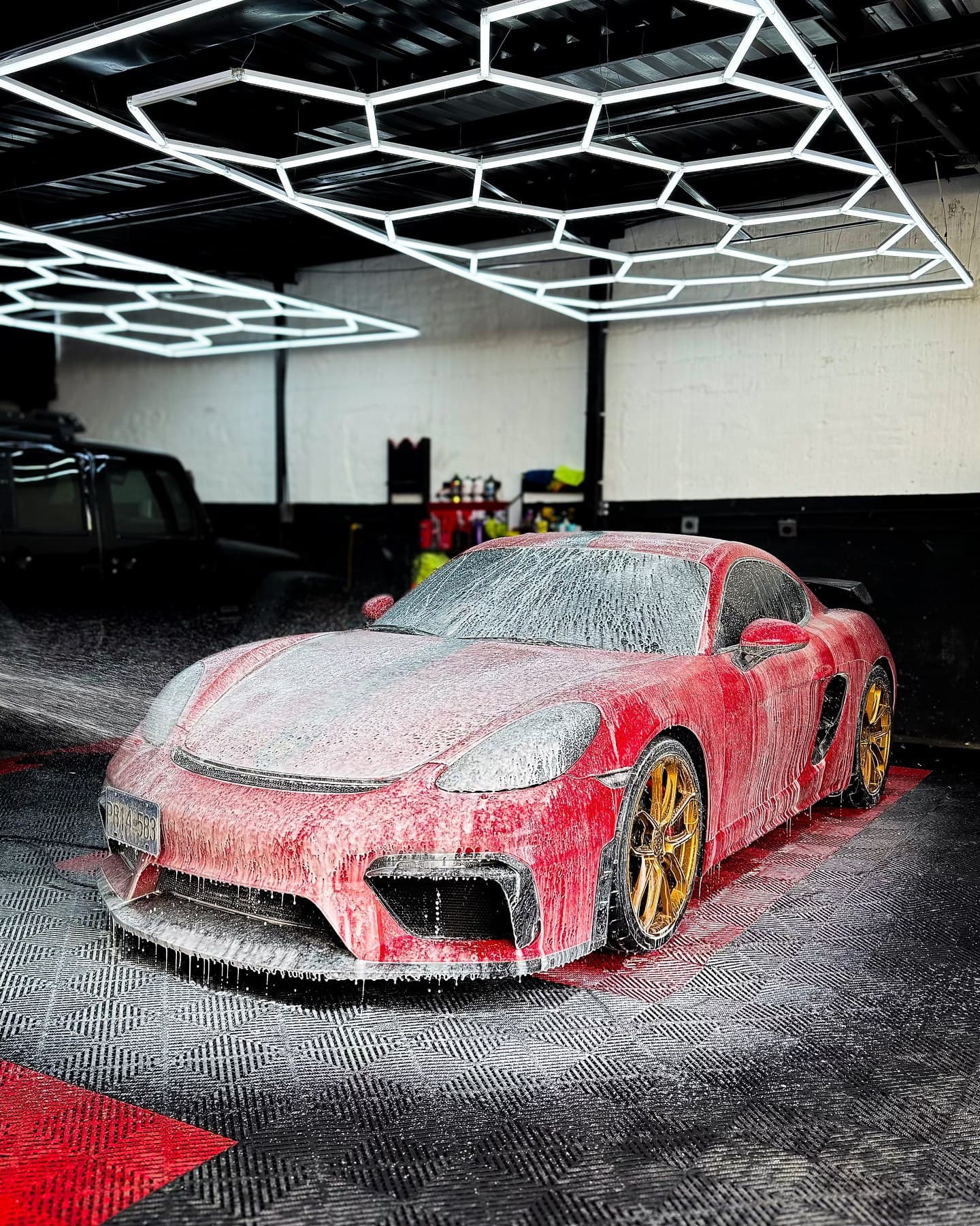 Porsche rojo con ruedas doradas cubierto de espuma en el taller bajo luces hexagonales